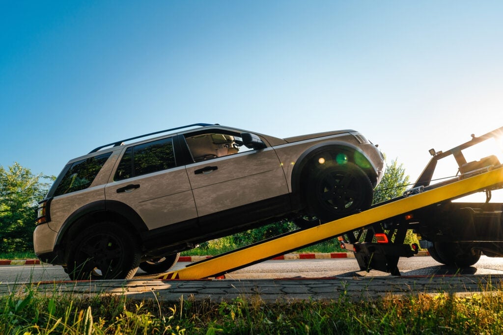 SUV loaded on a yellow tow truck flatbed during daytime with clear blue sky